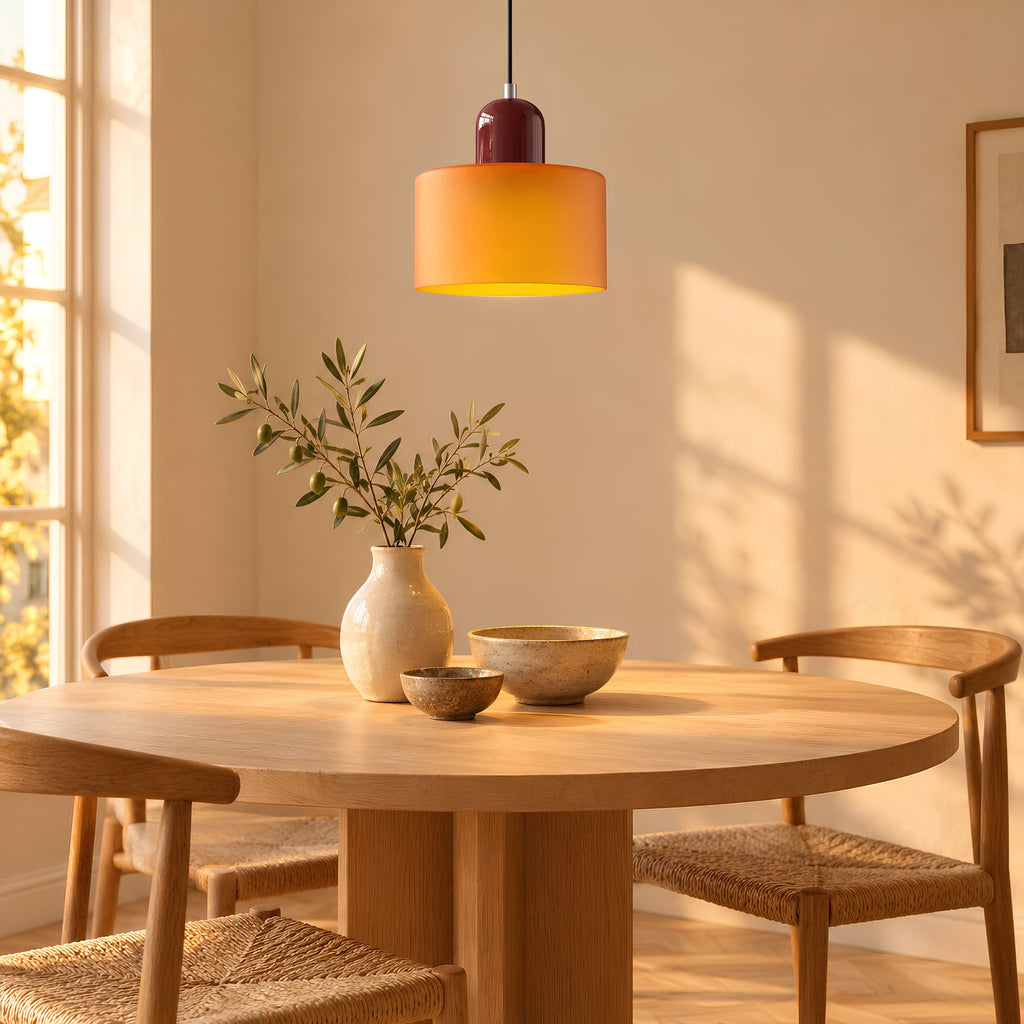Suspension MIRA abat-jour ambre et capuchon bordeaux, allumée au-dessus d'une table ronde en bois